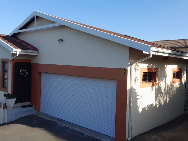 Front exterior view of the cluster home featuring a double garage, paved driveway, and neutral facade with contrasting trim.