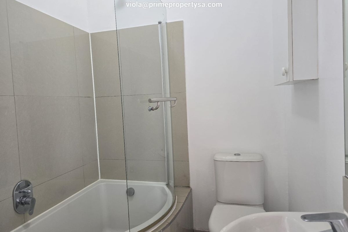 A functional bathroom featuring a shower-over-bath combination with a glass screen, a standard toilet, and a wall-mounted vanity basin.