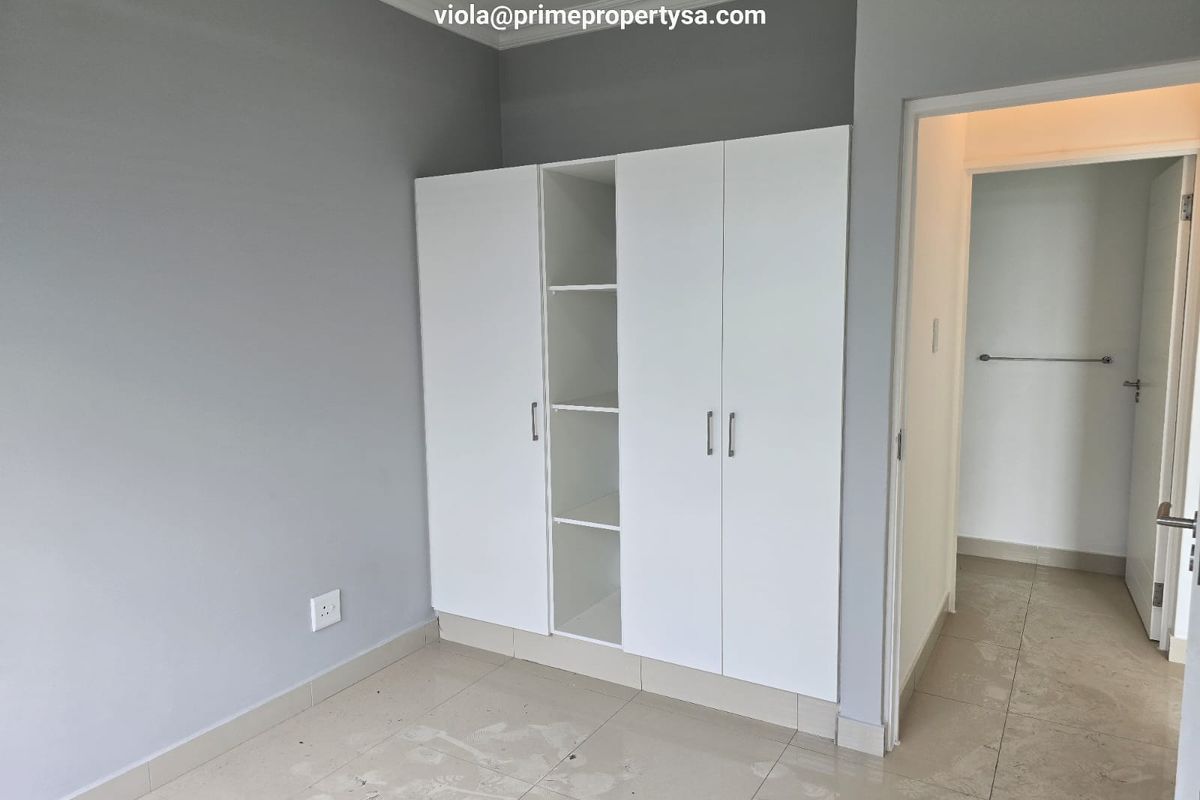 A bedroom featuring built-in white cabinetry with open shelving and tiled flooring, leading into an adjacent hallway.