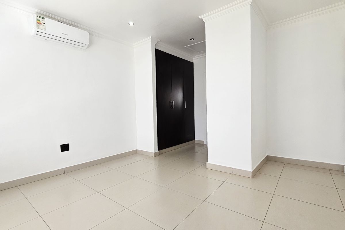 A bright, empty bedroom featuring neutral floor tiles, built-in dark wood cabinetry, and a wall-mounted air conditioning unit.
