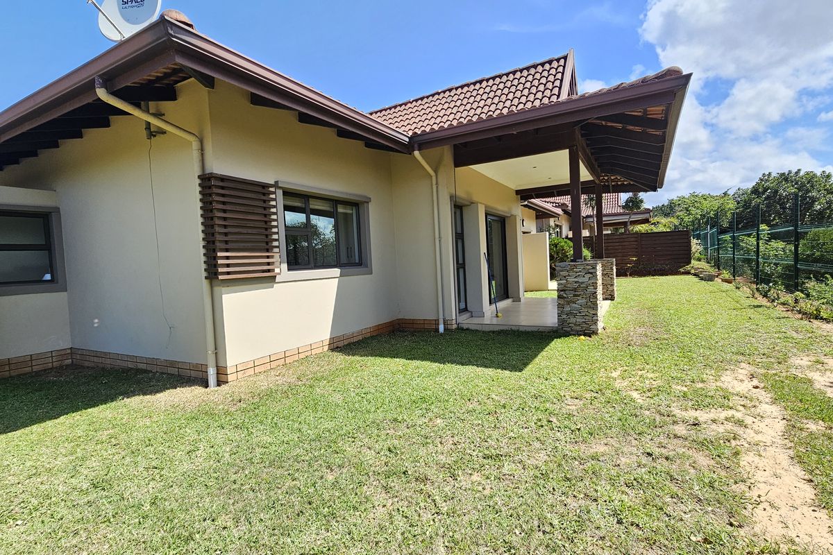 Rear view of the townhouse featuring a covered patio, tiled roof, and a private garden area enclosed by perimeter fencing.