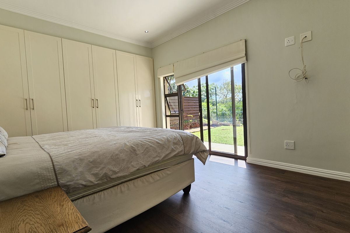 A bright bedroom featuring built-in cupboards, dark laminate flooring, and sliding glass doors providing direct access to the rear garden.