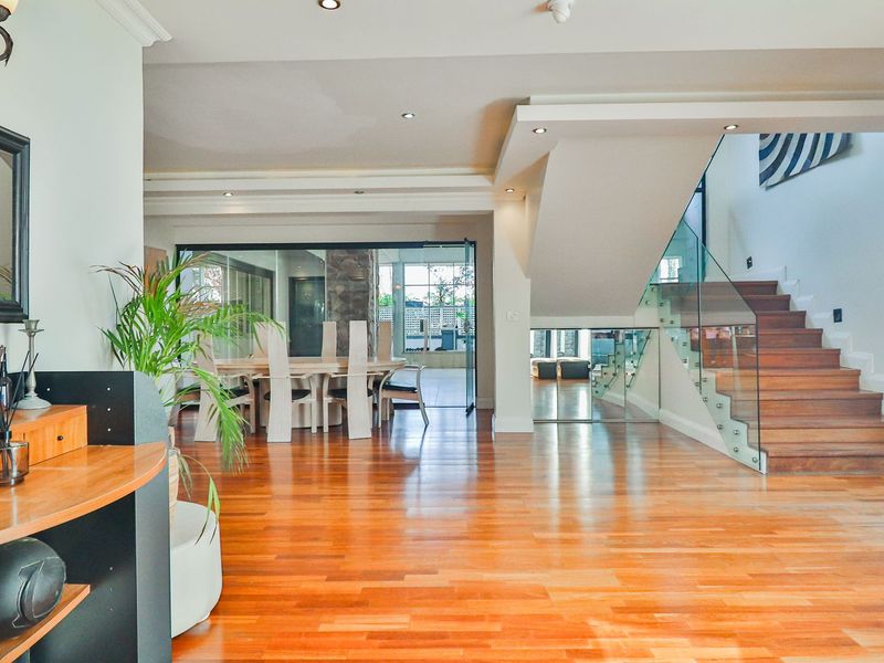 Spacious open-plan living area featuring polished hardwood flooring, a modern staircase with glass balustrades, and recessed lighting leading to a dining space.