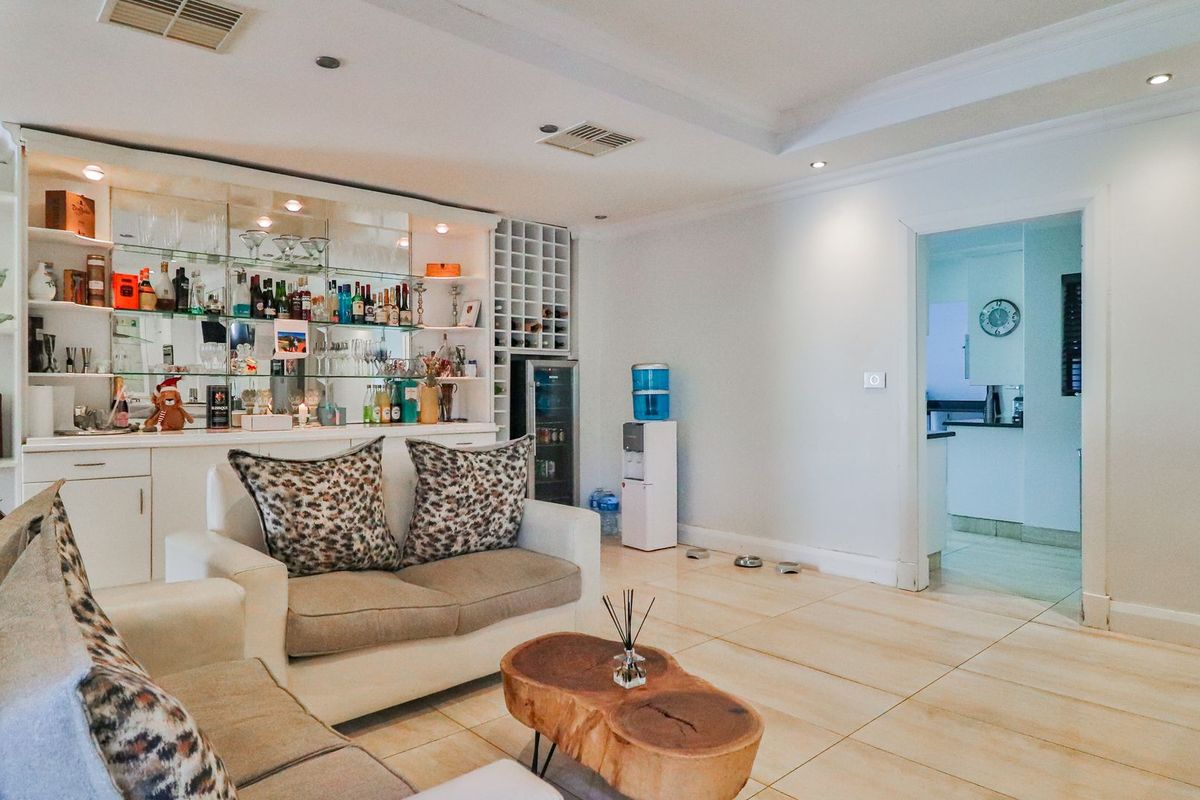 A comfortable living room featuring a built-in bar with glass shelving, wine storage, tiled flooring, and recessed lighting, with an adjacent view into the kitchen.