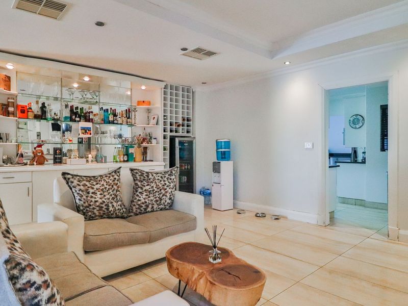 A comfortable living room featuring a built-in bar with glass shelving, wine storage, tiled flooring, and recessed lighting, with an adjacent view into the kitchen.