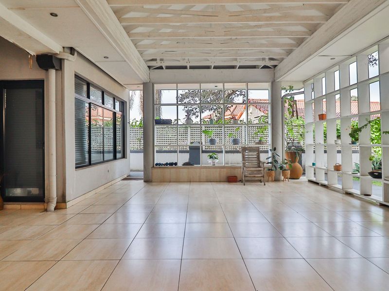 Spacious covered patio featuring large glass windows, tiled flooring, and a unique exposed beam ceiling, offering a bright and versatile outdoor living space.