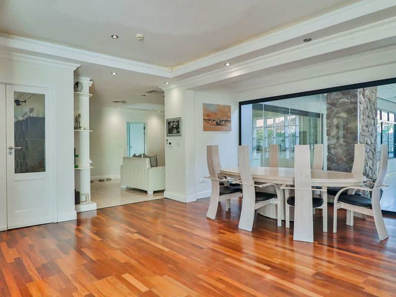 Spacious open-plan living and dining area featuring polished hardwood flooring, recessed lighting, and a striking stone feature wall with large glass sliding doors.