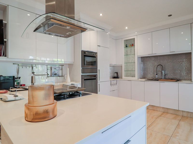 Modern kitchen featuring white high-gloss cabinetry, a central island with a gas hob, built-in appliances, and a stylish mosaic tile backsplash.
