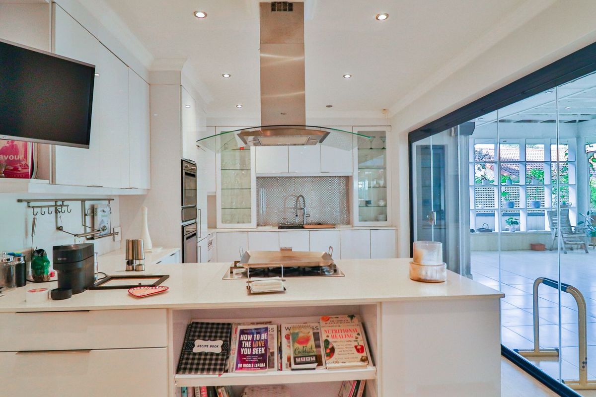 Modern kitchen featuring white cabinetry, a central island with a gas cooktop, stainless steel extractor fan, and seamless access to an outdoor patio area.