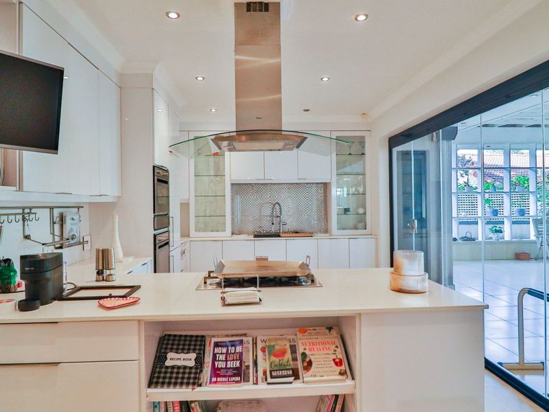 Modern kitchen featuring white cabinetry, a central island with a gas cooktop, stainless steel extractor fan, and seamless access to an outdoor patio area.