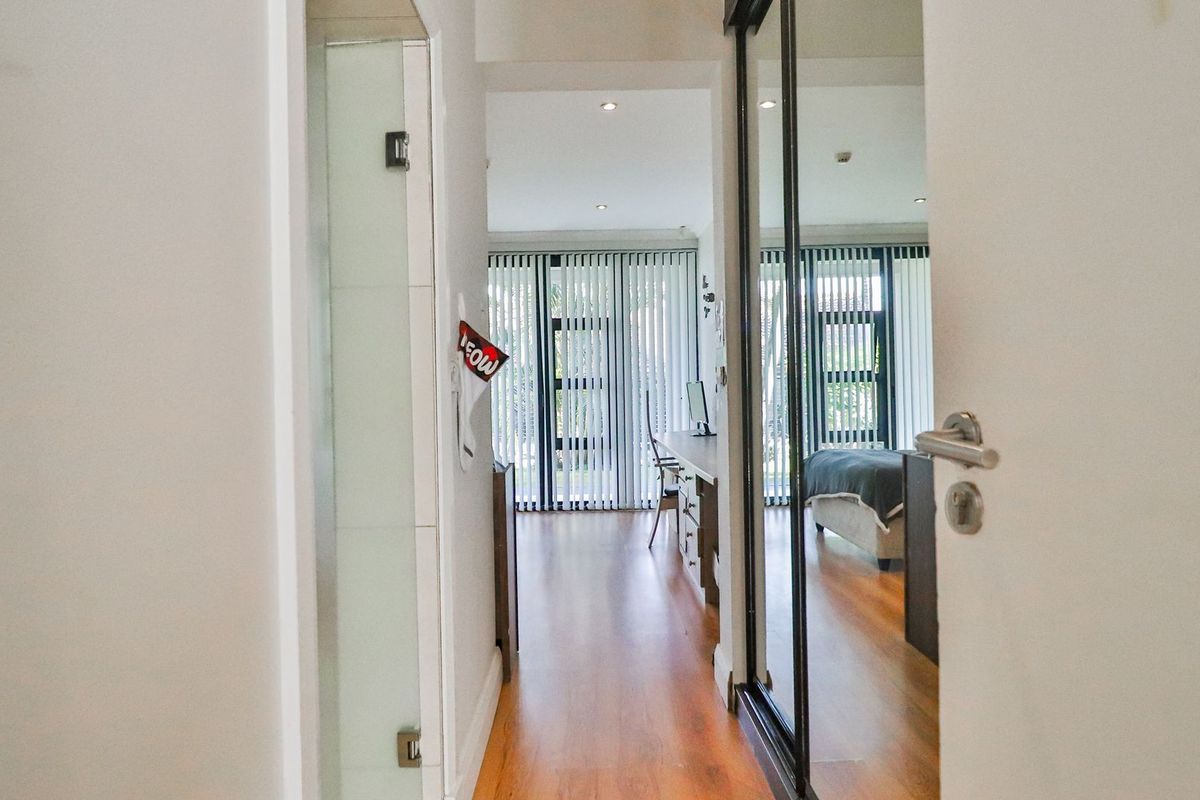 A bedroom featuring laminate flooring, built-in cupboards with mirrored sliding doors, and vertical blinds, viewed from the doorway.