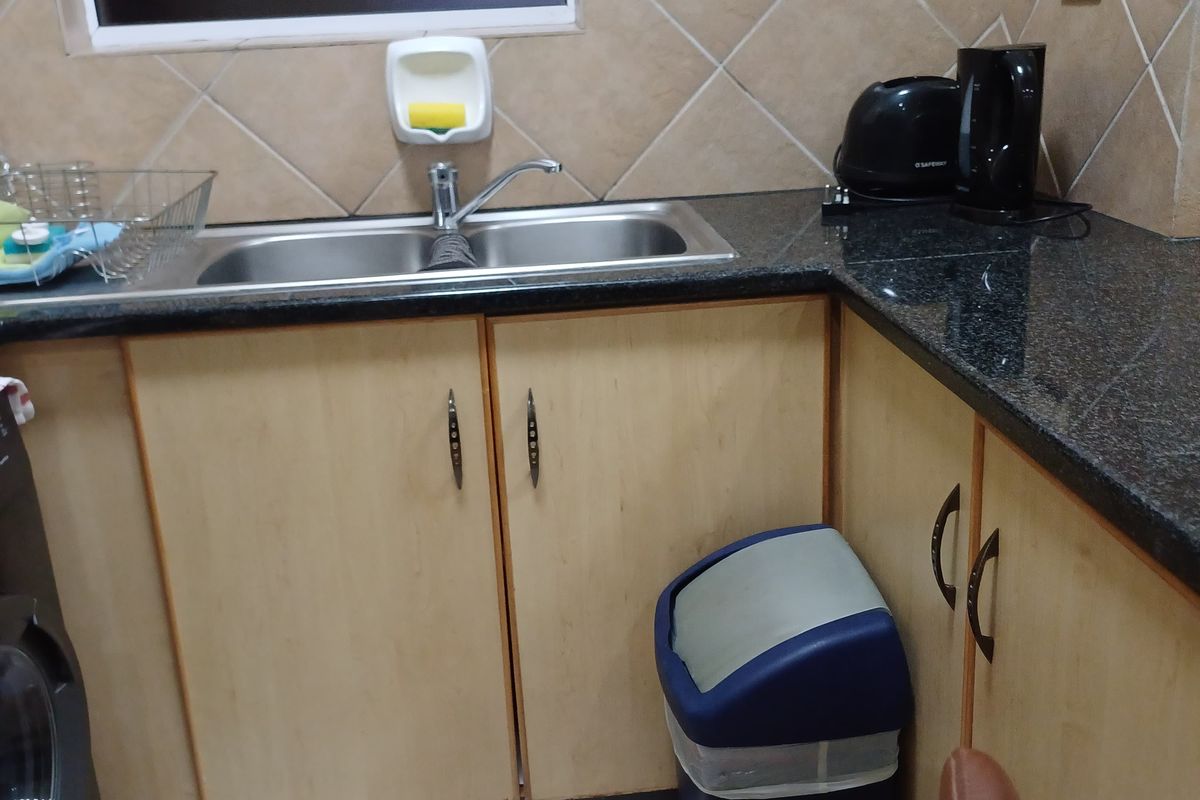 A functional kitchen area featuring granite countertops, light wood cabinetry, a double stainless steel sink, and tiled splashbacks.