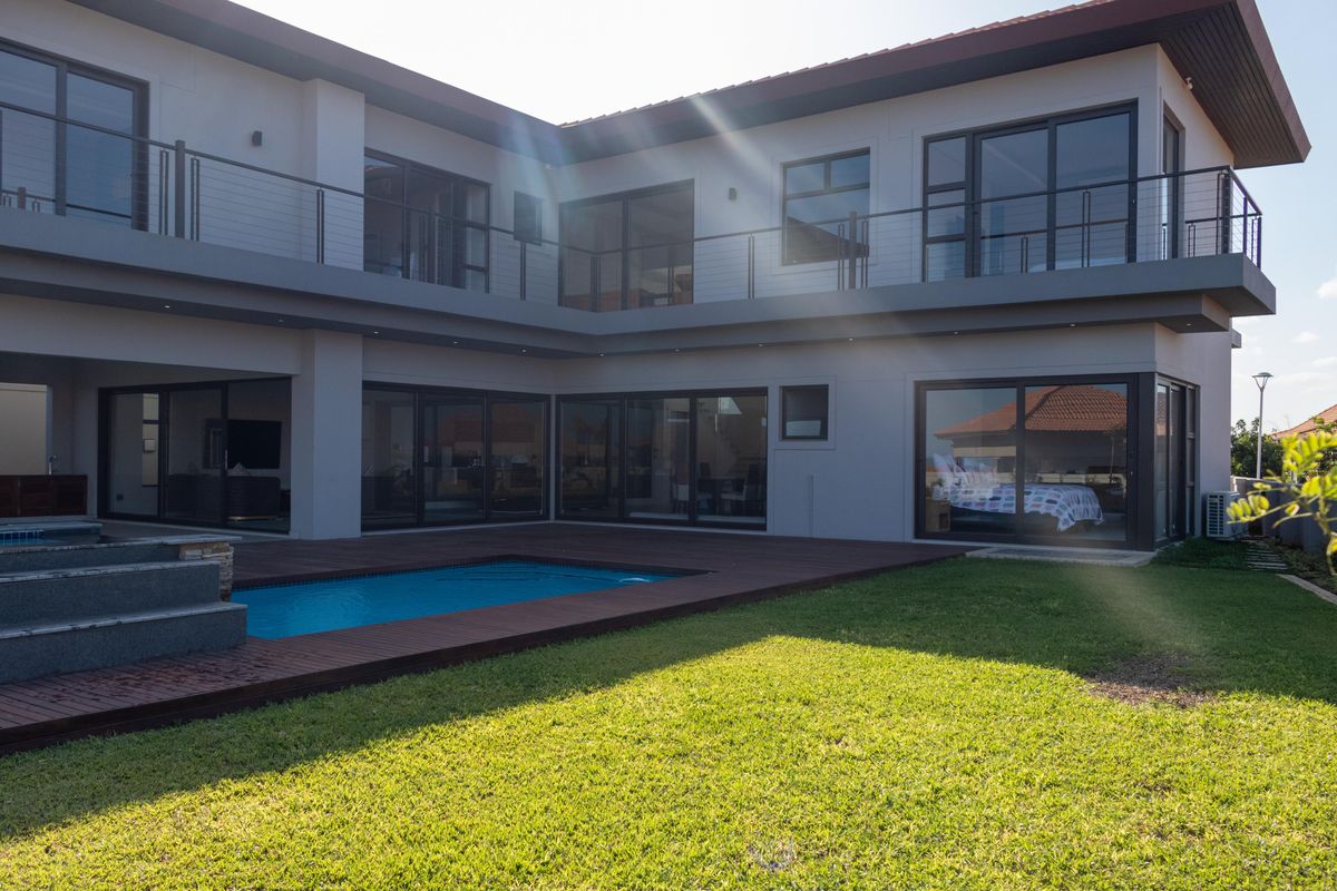 Modern double-story residence featuring a swimming pool, timber decking, expansive glass sliding doors, and a spacious upper-level balcony overlooking the rear garden.