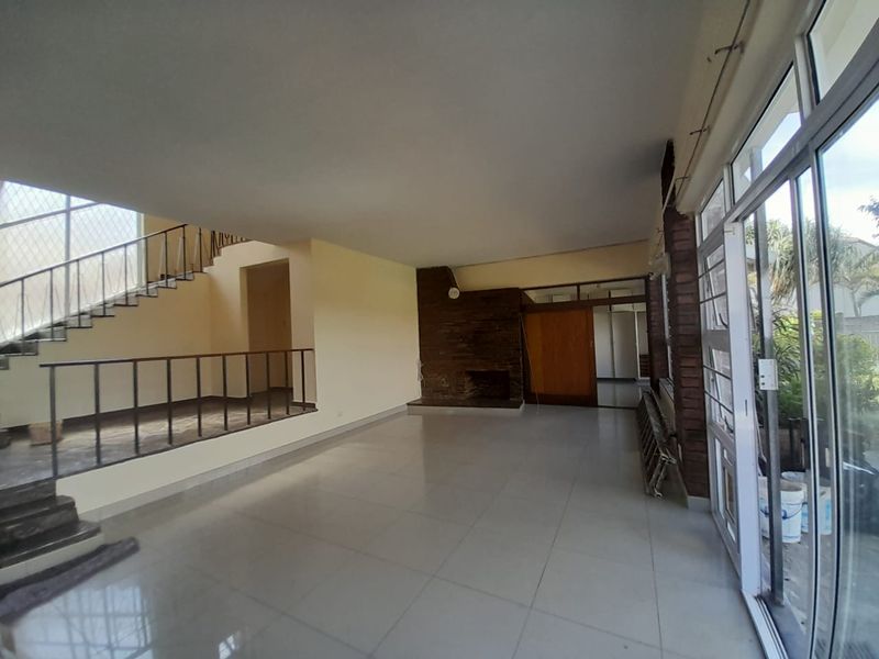 Spacious open-plan living area featuring a brick fireplace, tiled flooring, and a staircase with metal balustrades, leading out to the garden through sliding doors.