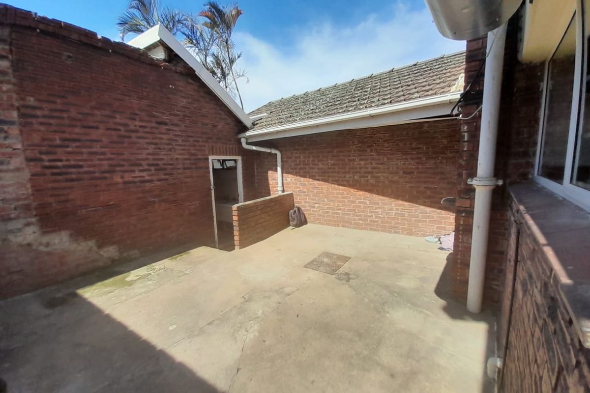 A rear exterior courtyard area featuring exposed brick walls, concrete paving, and traditional roof tiling, requiring maintenance and potential cosmetic upgrades.