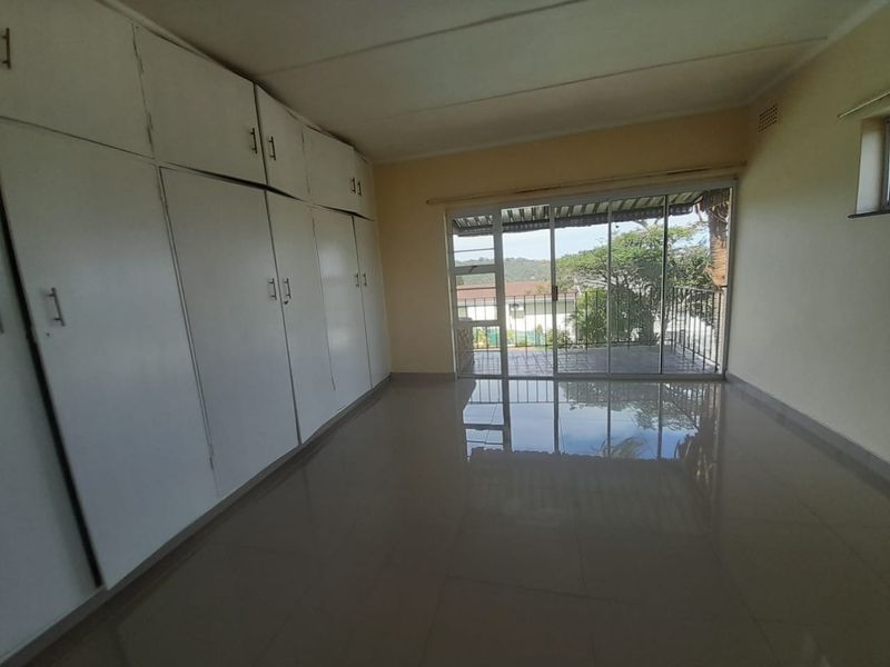 An empty bedroom featuring extensive built-in cupboards, tiled flooring, and a sliding glass door providing access to a balcony with outdoor views.