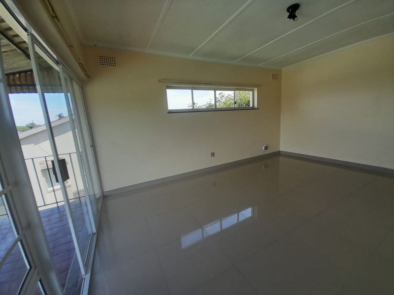A bright, empty living room featuring large sliding glass doors leading to a balcony, neutral tiled flooring, and a horizontal window.