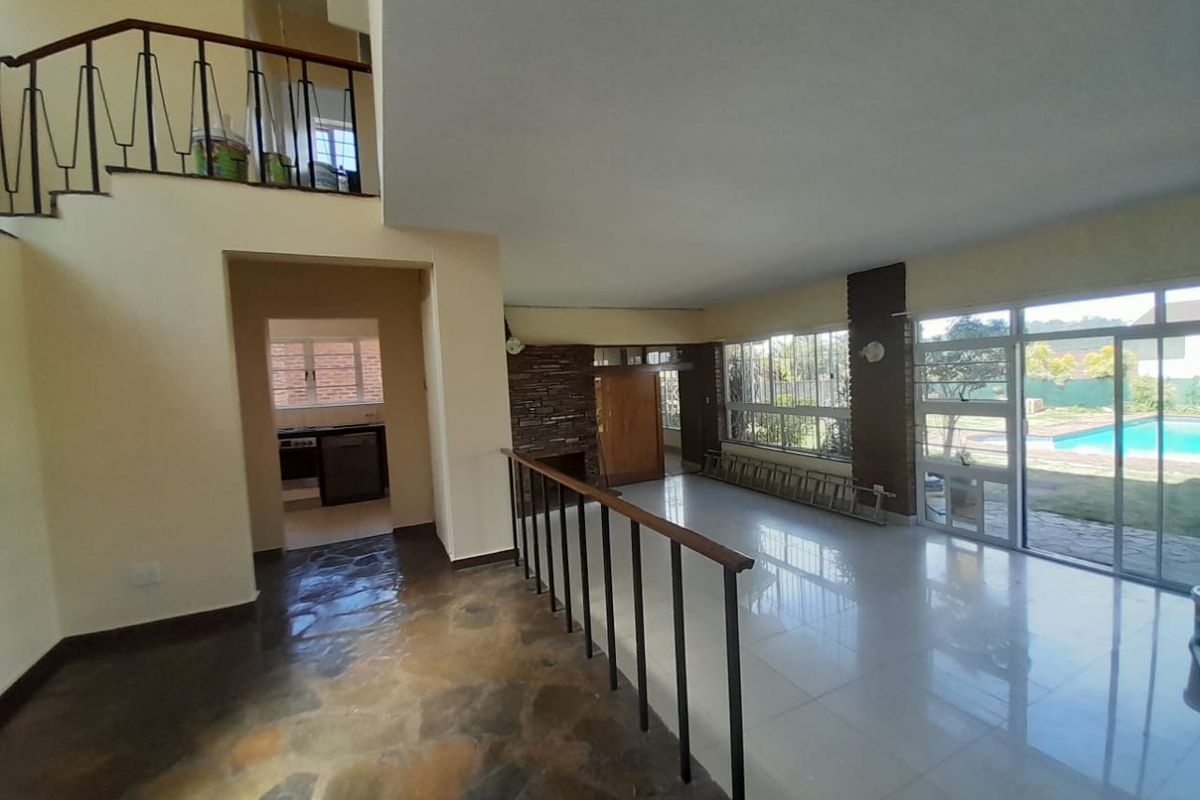 Spacious open-plan living area featuring a stone fireplace, split-level flooring, and large sliding glass doors providing direct access to the pool area.