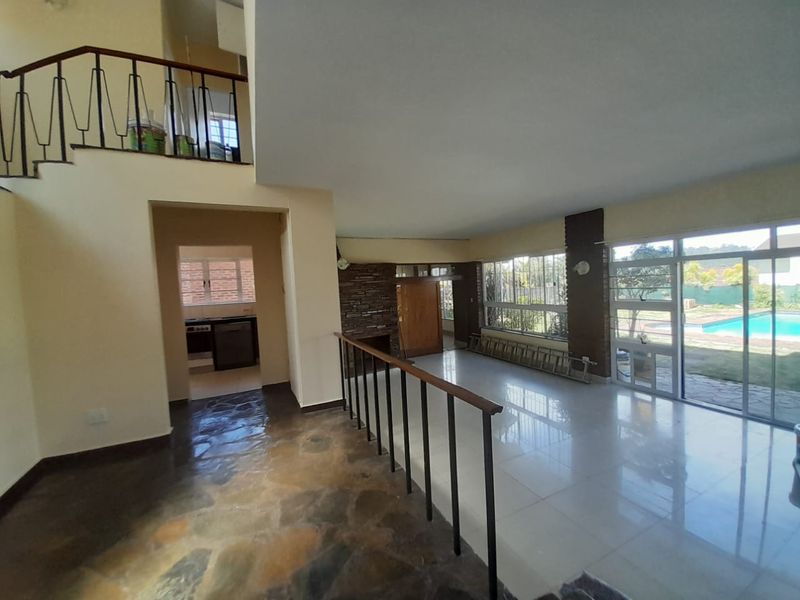 Spacious open-plan living area featuring a stone fireplace, split-level flooring, and large sliding glass doors providing direct access to the pool area.