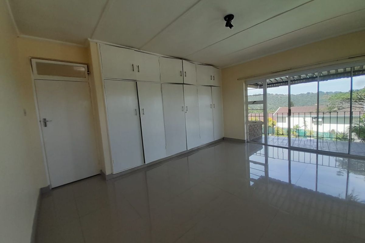Spacious bedroom featuring extensive built-in cupboards, tiled flooring, and large sliding glass doors providing access to an outdoor area.
