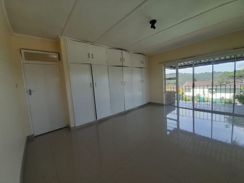 Spacious bedroom featuring extensive built-in cupboards, tiled flooring, and large sliding glass doors providing access to an outdoor area.