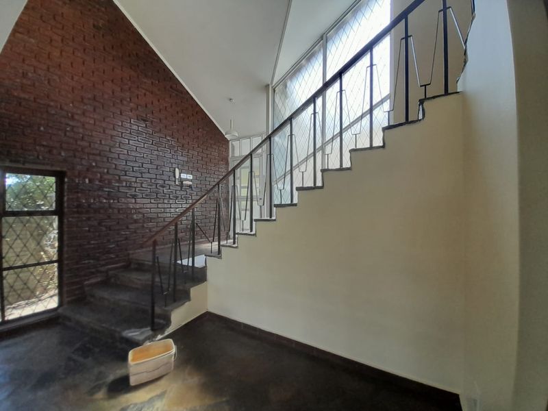 Spacious entrance hallway featuring an exposed brick wall, vaulted ceiling, and a staircase with a metal balustrade.