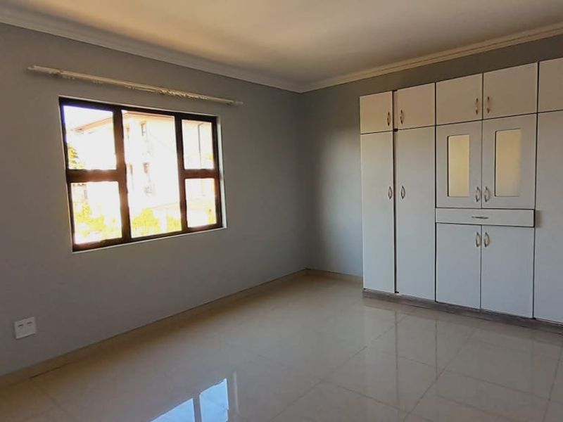A bright, empty bedroom featuring neutral grey walls, large built-in cupboards, and clean tiled flooring.