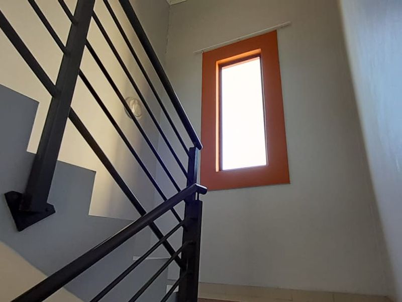 A bright stairwell featuring a modern metal balustrade and a tall vertical window, providing natural light to the transition area between floors.