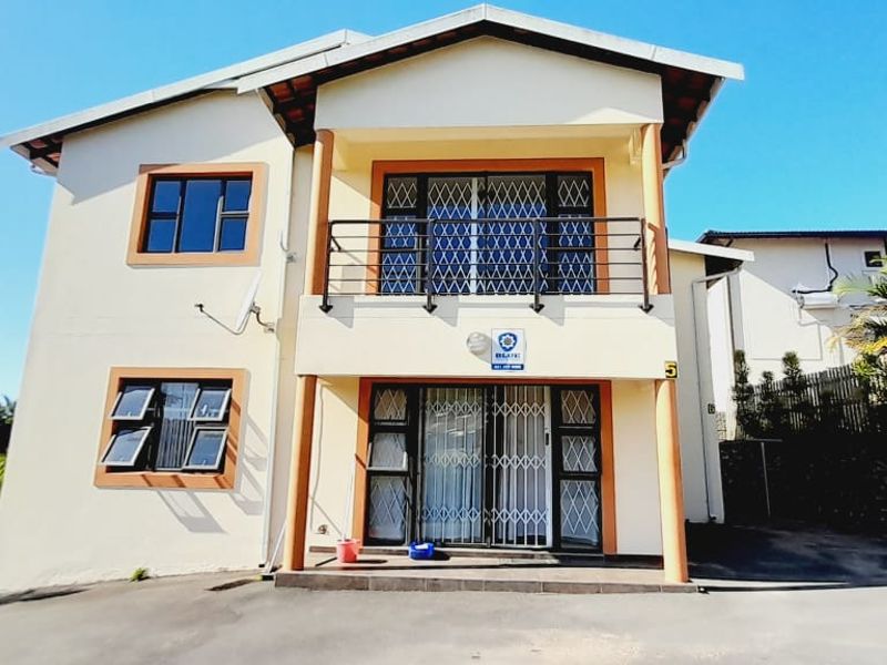 Front elevation of a two-story townhouse featuring a balcony, security gates, and a paved driveway area.