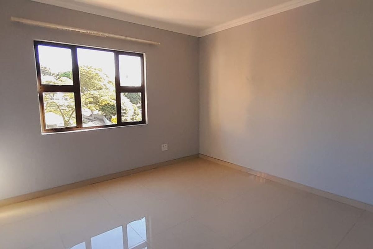 A bright, empty bedroom featuring neutral tiled flooring, built-in cupboards, and a large window providing natural light.
