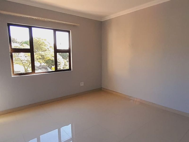 A bright, empty bedroom featuring neutral tiled flooring, built-in cupboards, and a large window providing natural light.