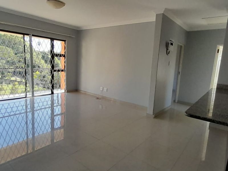 An open-plan living area featuring tiled flooring, a granite kitchen countertop, and a large sliding glass door with security gate leading to the exterior.