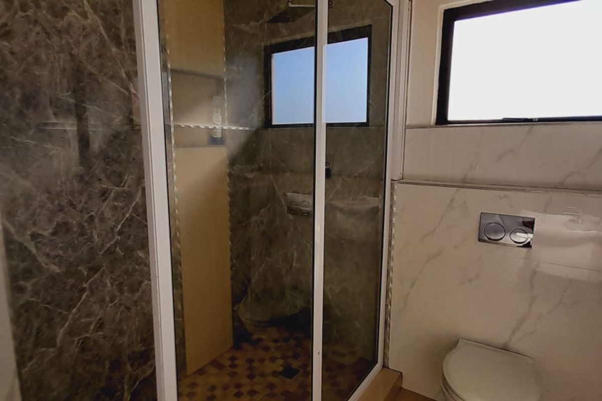 Modern bathroom featuring a walk-in shower with glass enclosure, marble-effect wall tiling, and a wall-mounted toilet.
