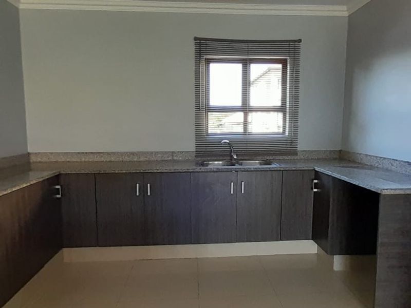A functional kitchen featuring dark wood cabinetry, granite countertops, a stainless steel sink, and tiled flooring in a clean, empty space.