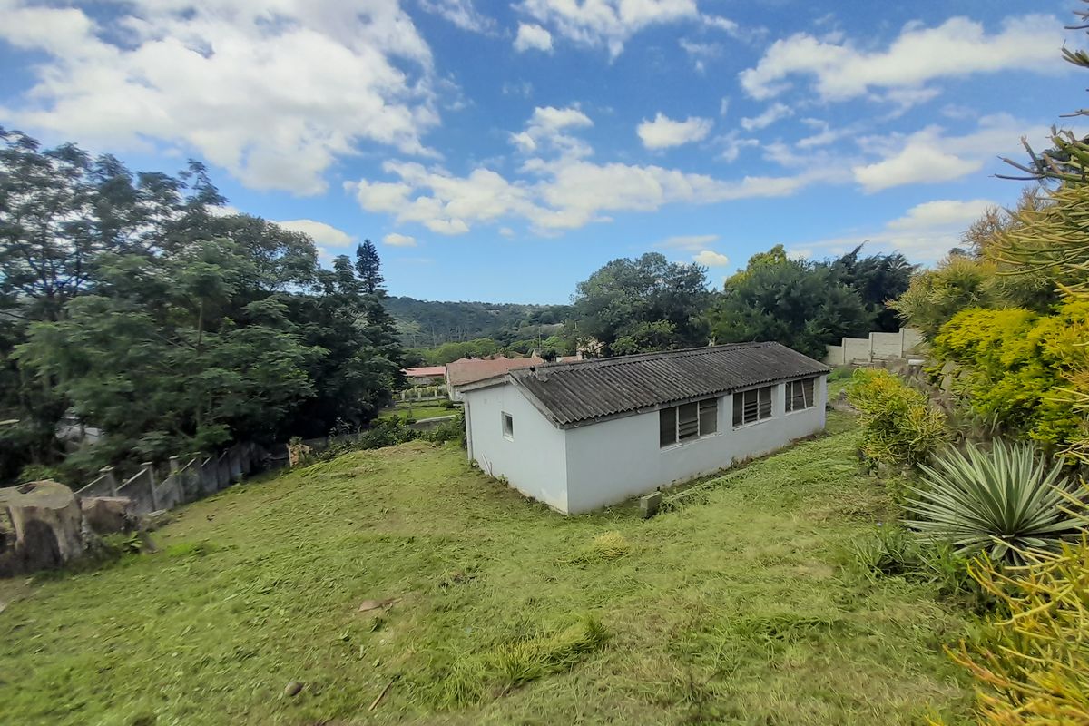 A rear view of a detached outbuilding or townhouse structure set within a large, sloped garden area with mature trees and boundary fencing.