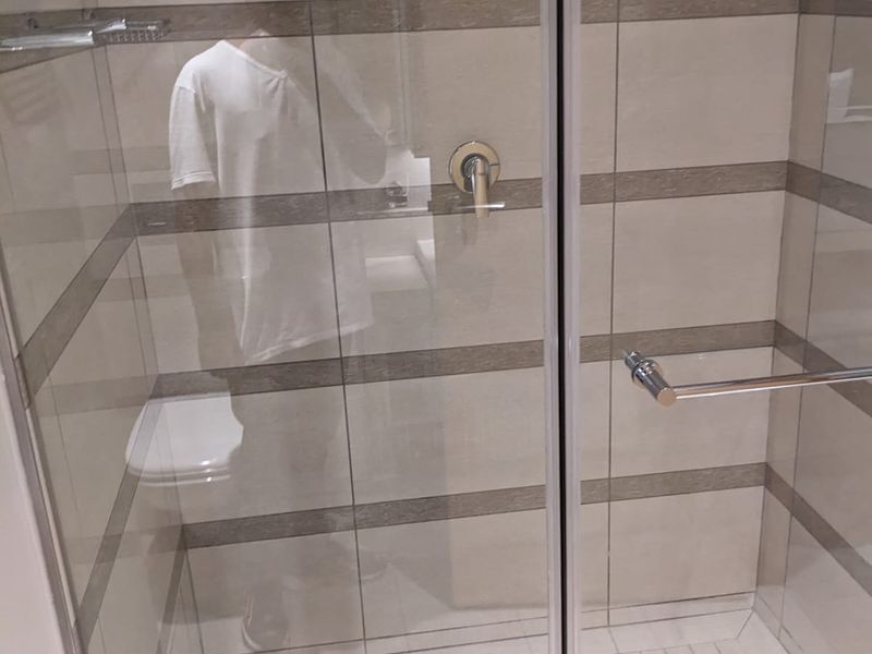 A modern walk-in shower featuring neutral-toned tiled walls, a glass enclosure, and a chrome shower mixer.