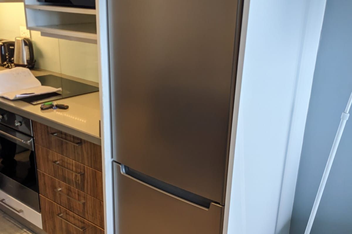 A modern kitchen featuring wood-grain cabinetry, stone countertops, a built-in oven, electric cooktop, and a stainless steel integrated refrigerator.