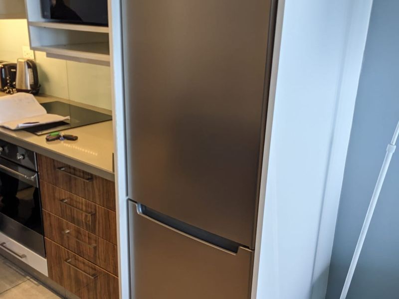 A modern kitchen featuring wood-grain cabinetry, stone countertops, a built-in oven, electric cooktop, and a stainless steel integrated refrigerator.