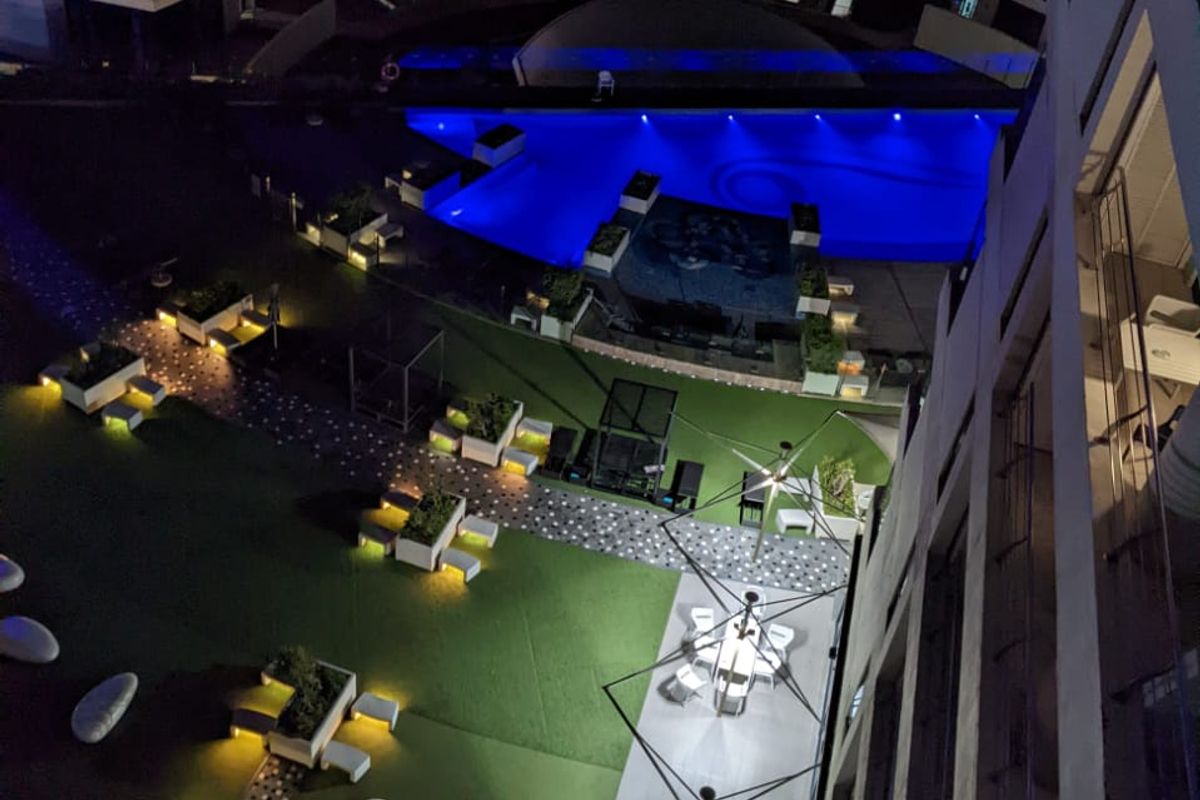 Elevated night view of the apartment complex featuring a illuminated swimming pool, landscaped garden areas, and paved outdoor communal spaces.