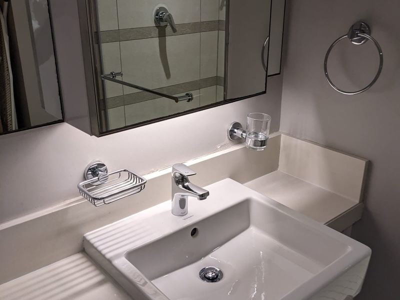 A clean and modern bathroom vanity area featuring a white basin, chrome fixtures, and a mirrored medicine cabinet with integrated lighting.