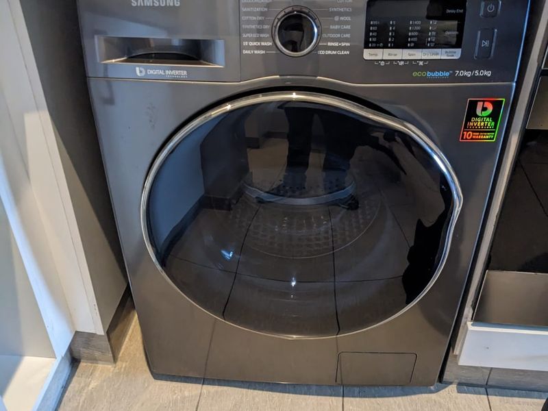 A built-in Samsung front-loading washing machine integrated under a stone countertop in a tiled laundry area.