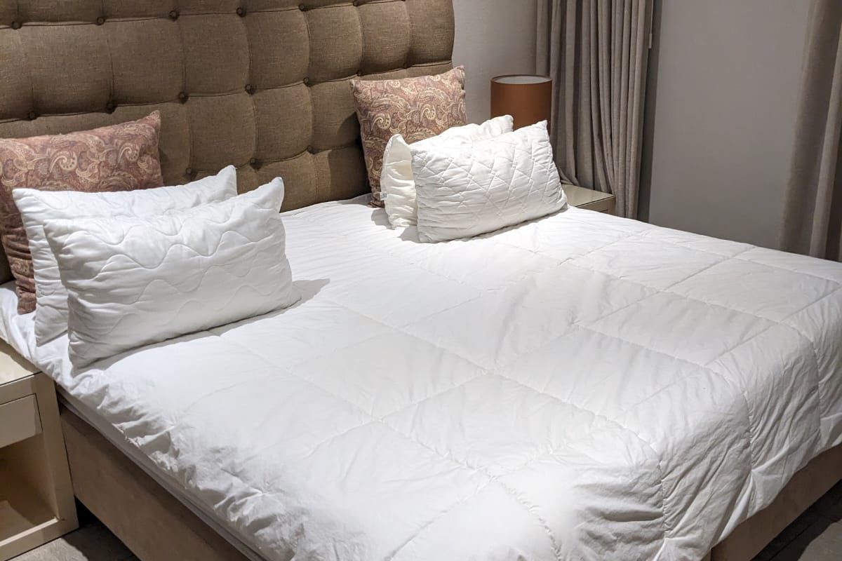 A well-maintained bedroom featuring neutral tiled flooring, a high-level window with full-length curtains, and a neutral color palette.