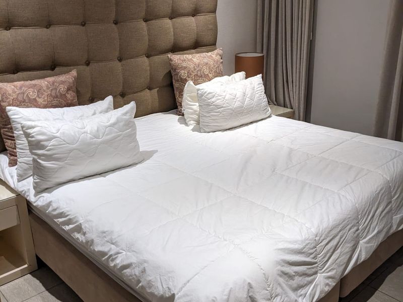 A well-maintained bedroom featuring neutral tiled flooring, a high-level window with full-length curtains, and a neutral color palette.