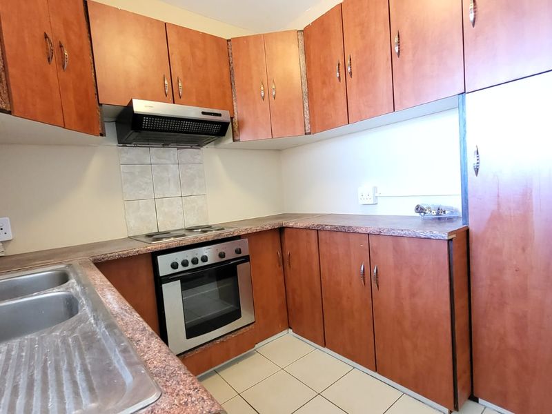 A functional kitchen featuring wood-look cabinetry, laminate countertops, a built-in oven with hob, and a stainless steel double sink.