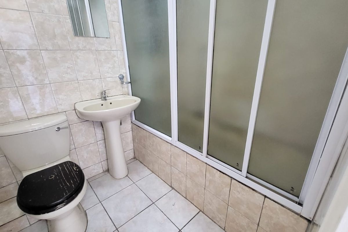 A functional bathroom featuring a pedestal basin, toilet, and a shower enclosure with sliding doors, finished with neutral wall and floor tiling.