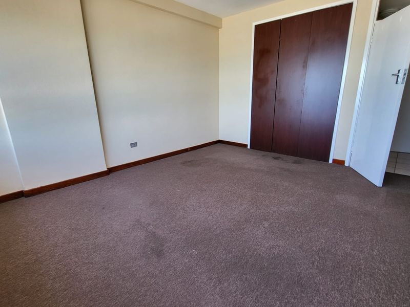 An empty bedroom featuring neutral walls, dark carpet flooring, and a built-in wardrobe with dark wood-finish doors.