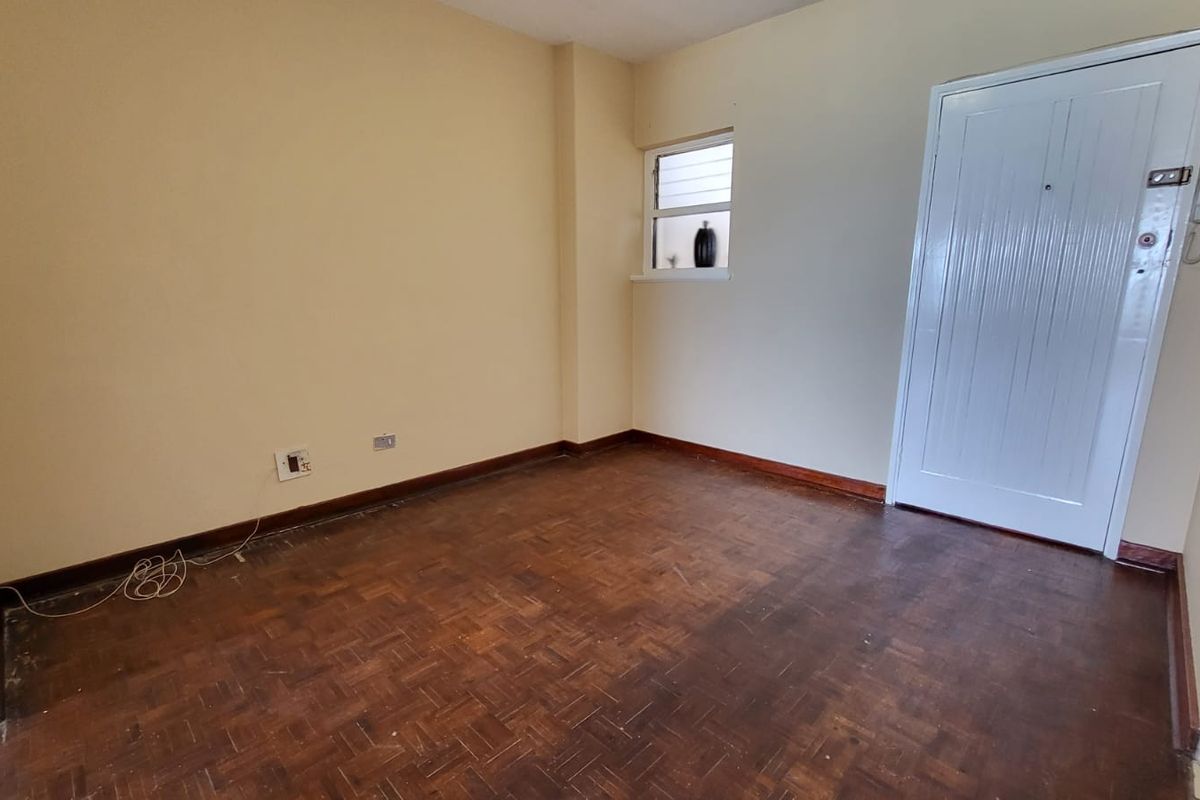 An empty bedroom featuring original parquet flooring, timber skirting boards, and a secure entrance door with an integrated intercom system.