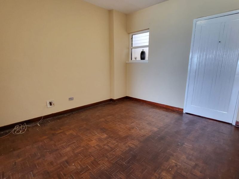An empty bedroom featuring original parquet flooring, timber skirting boards, and a secure entrance door with an integrated intercom system.