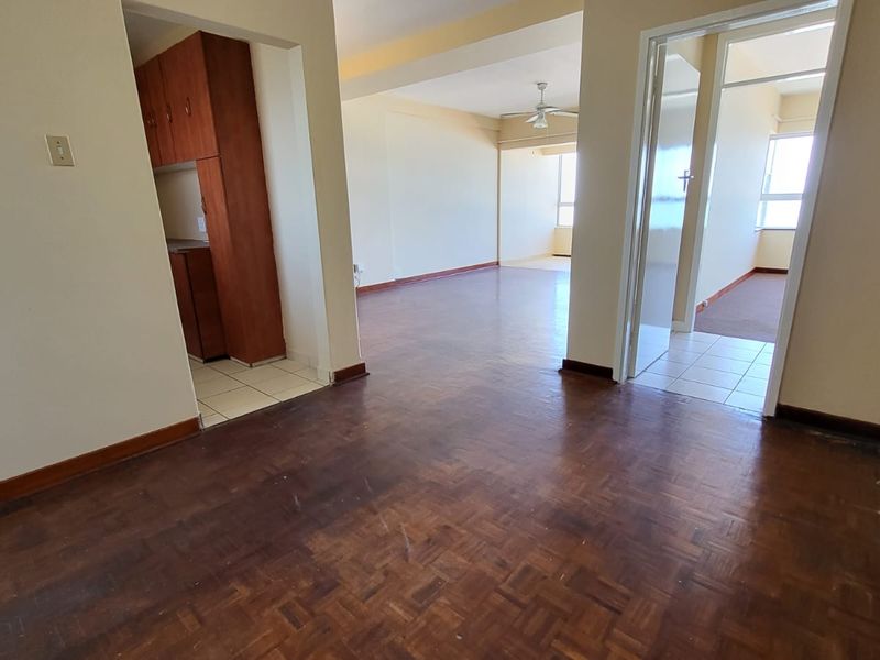 An open-plan living area featuring original parquet flooring, connected to a kitchen space and adjacent rooms with neutral wall finishes.