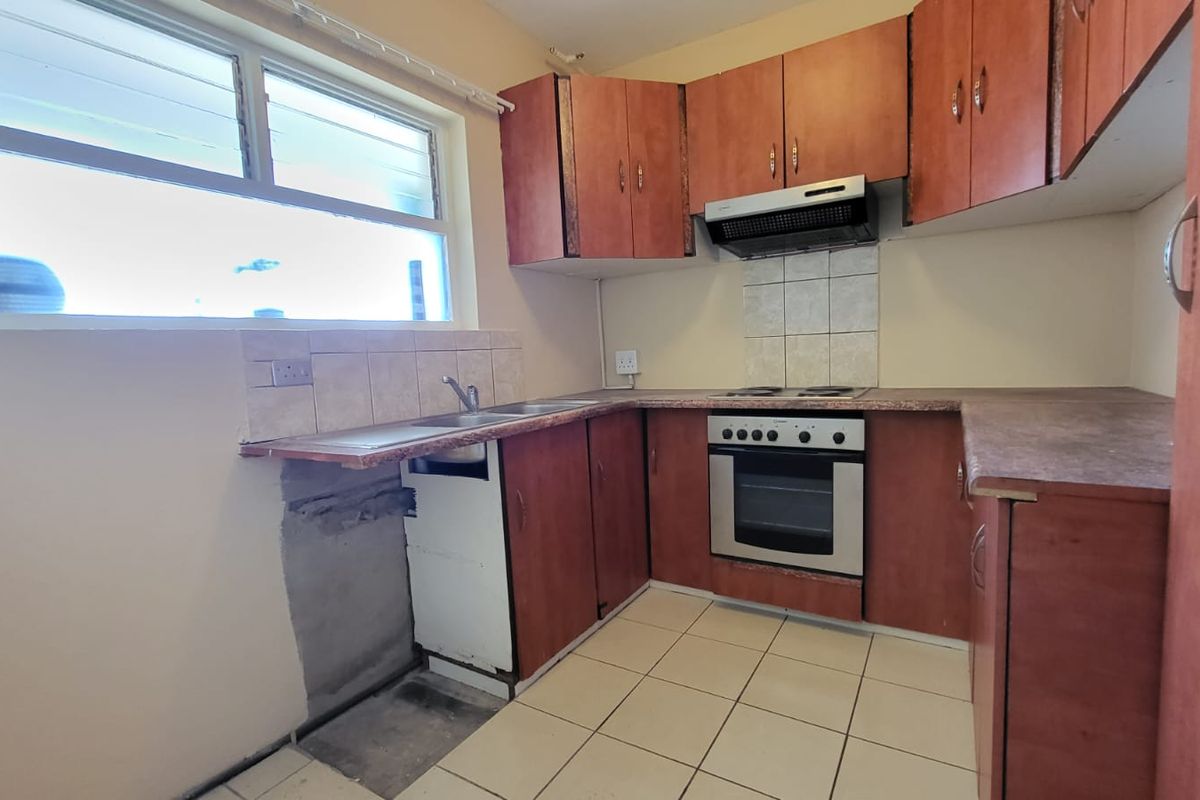A functional kitchen featuring laminate cabinetry, built-in oven, hob, and extractor fan, with tiled flooring and splashback. Requires minor repairs to base cabinetry.